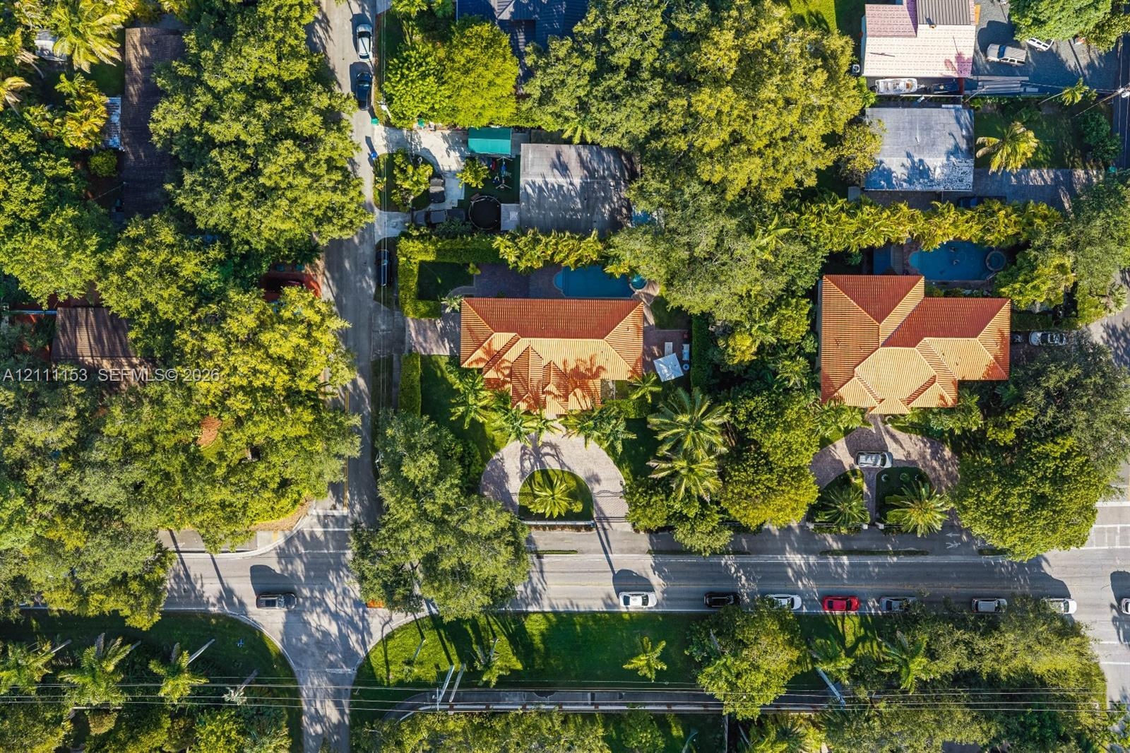 Aerial perspective of a property featuring a tiled roof, circular driveway, swimming pool, and dense perimeter landscaping