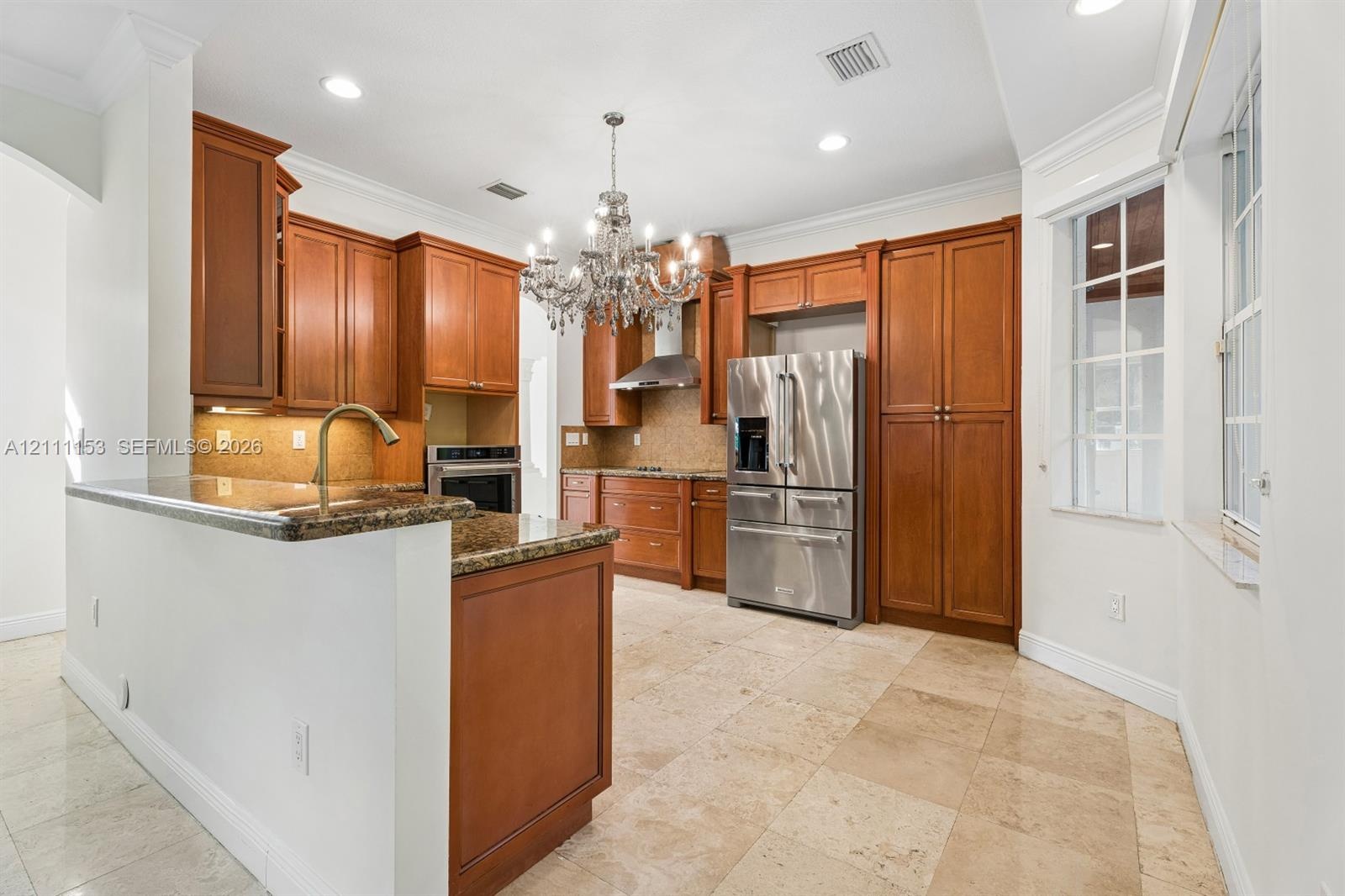 Kitchen featuring wood cabinetry, stone countertops, stone flooring, stainless steel appliances, and a chandelier