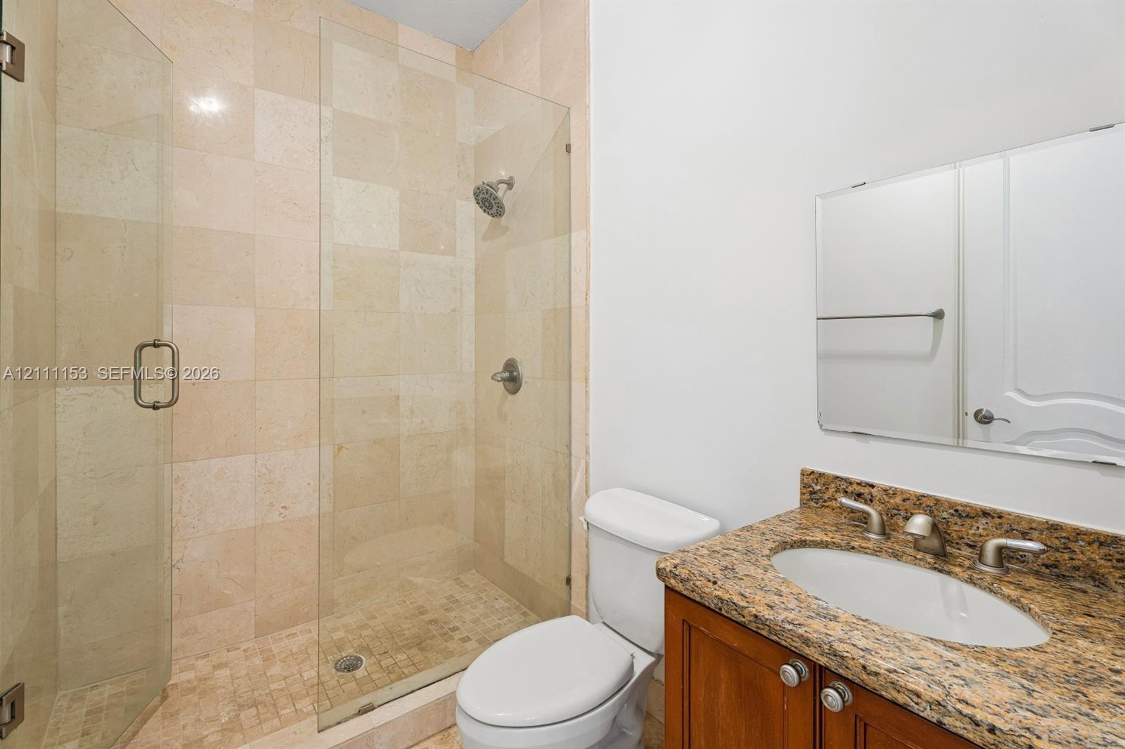 Walk-in shower featuring glass enclosure, stone tile wall surround, and stone tile flooring, accented by a vanity with stone countertop and an oval dr