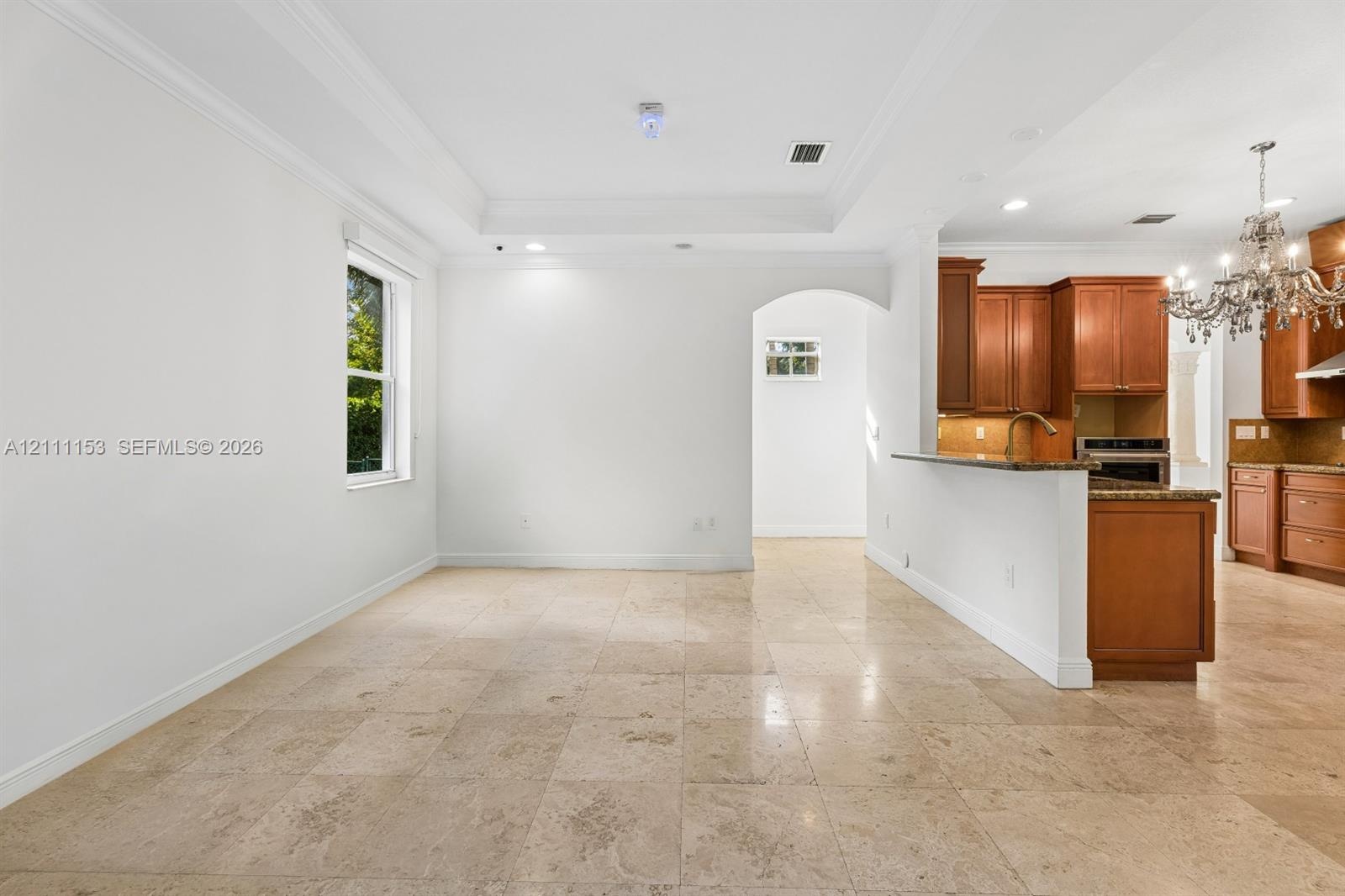 Tray ceiling with crown molding, stone tile flooring, arched entryway, wooden cabinetry, and peninsula-style countertop