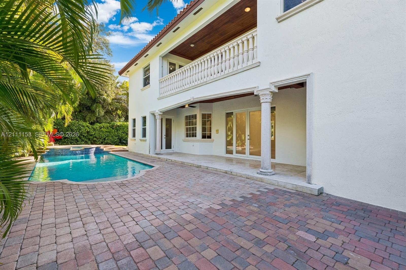 Stucco exterior featuring a second-story balcony with balustrades, a covered patio with columns, wood-paneled ceiling, and a paver pool deck