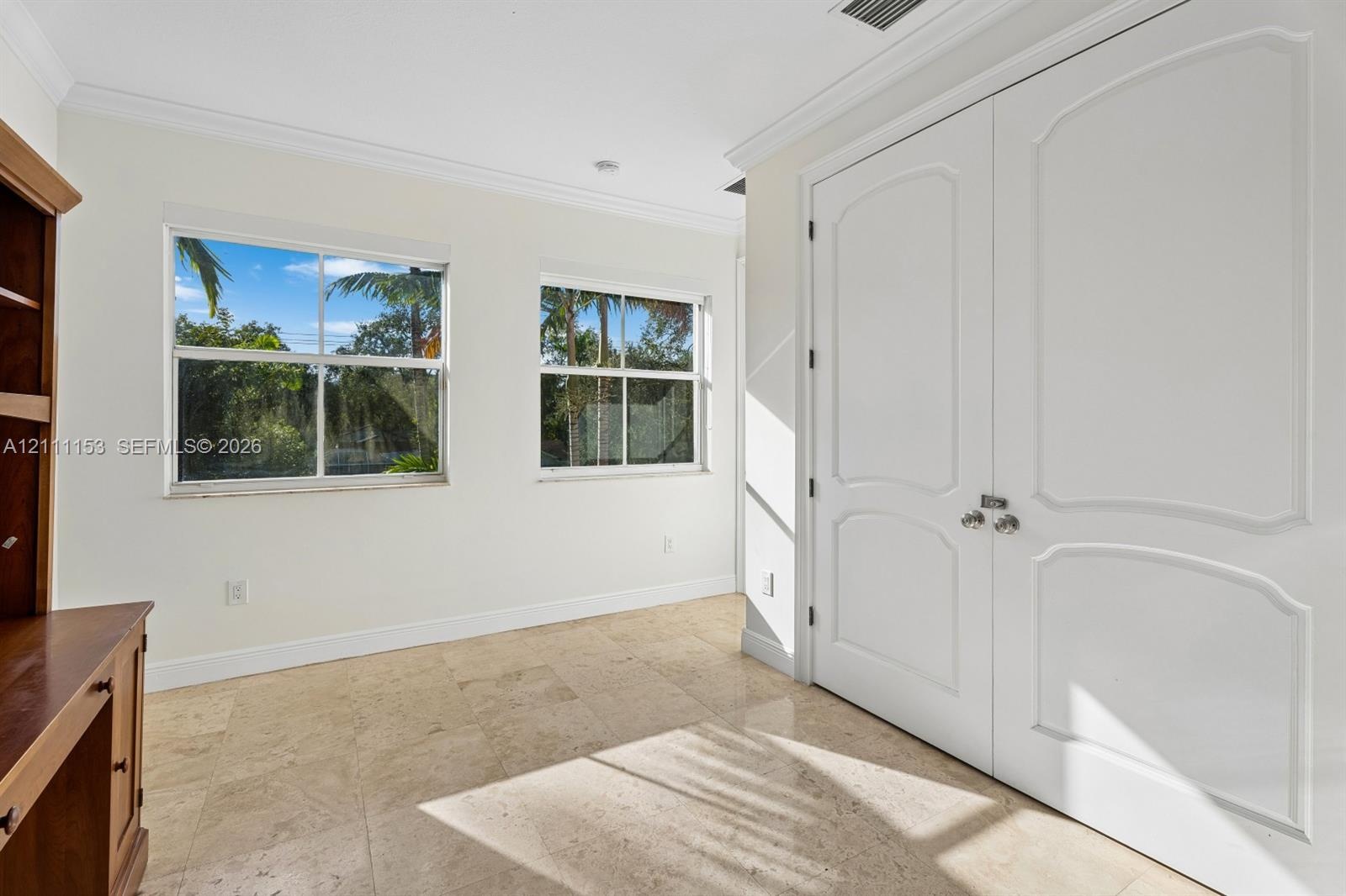 Room featuring stone flooring, dual-panel white doors, crown molding, and two windows