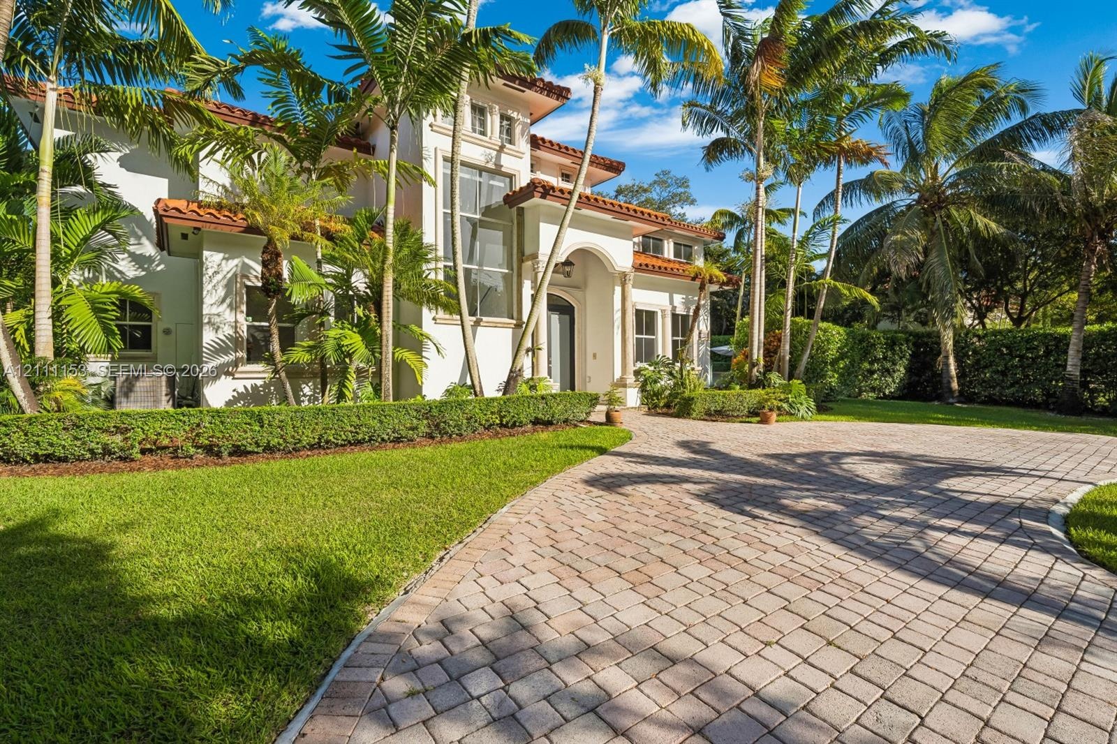 Mediterranean-style residence featuring a stucco facade, red tile roof, arched entryway with decorative columns, and an expansive paved driveway