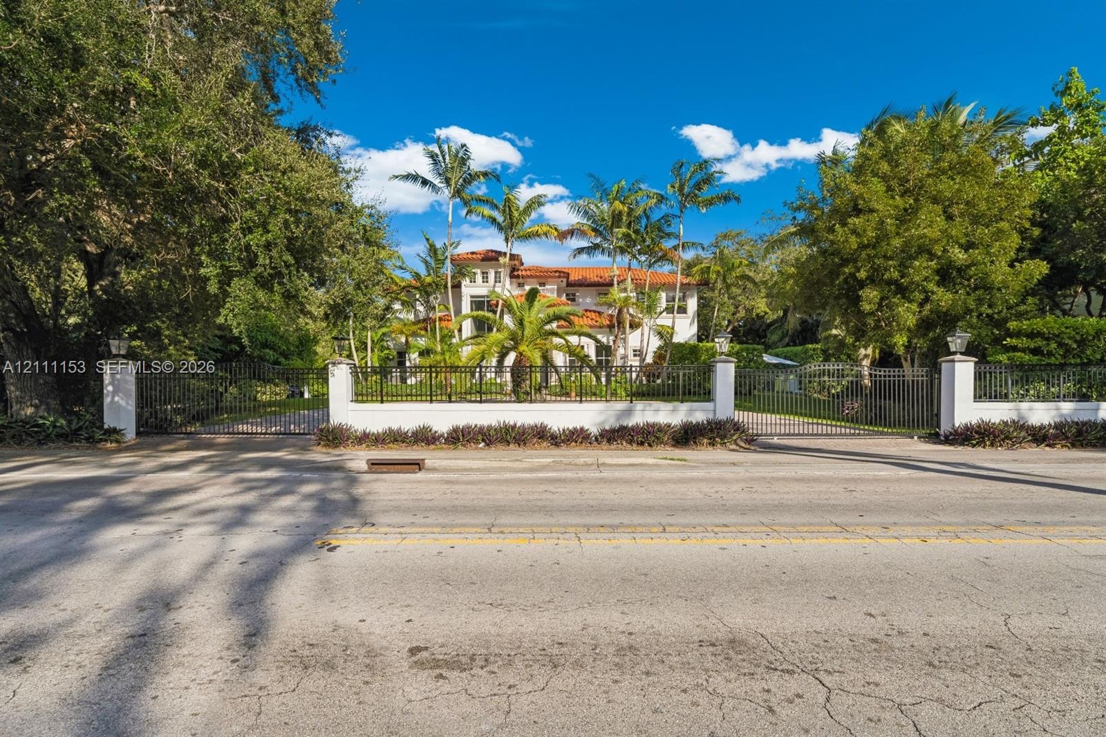 Multi-story residence featuring a terracotta tile roof, enclosed by a gated perimeter wall with decorative stone pillars, black metal fencing, and mat