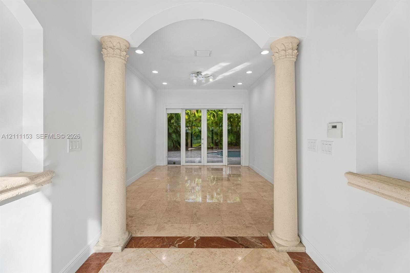 Entryway featuring arched architectural details, decorative stone columns, polished stone flooring with inlaid border, recessed lighting, and glass pa