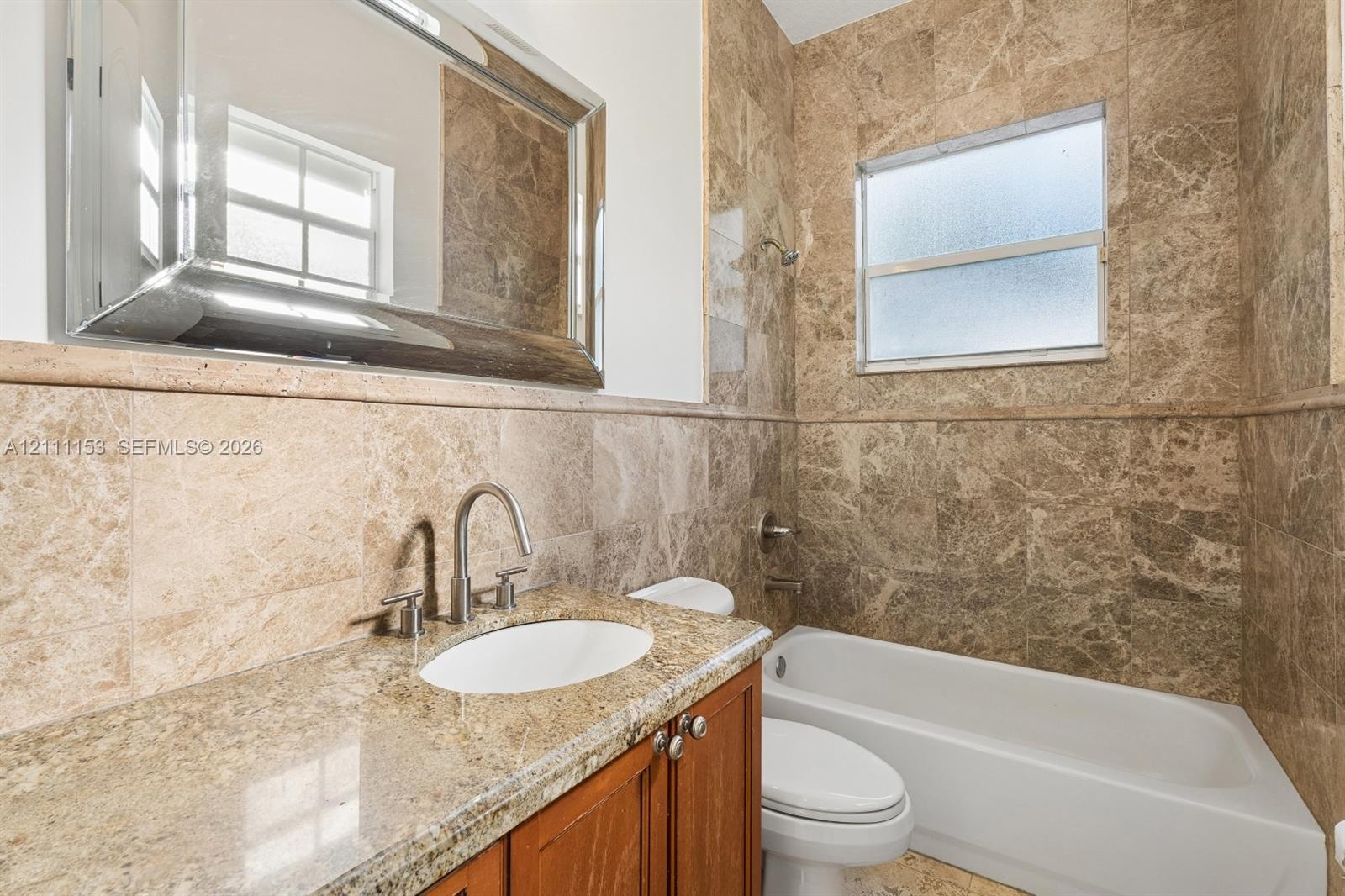 Stone-surround bathtub, vanity with stone countertop, undermount sink, brushed nickel faucet, and wood-finish cabinetry