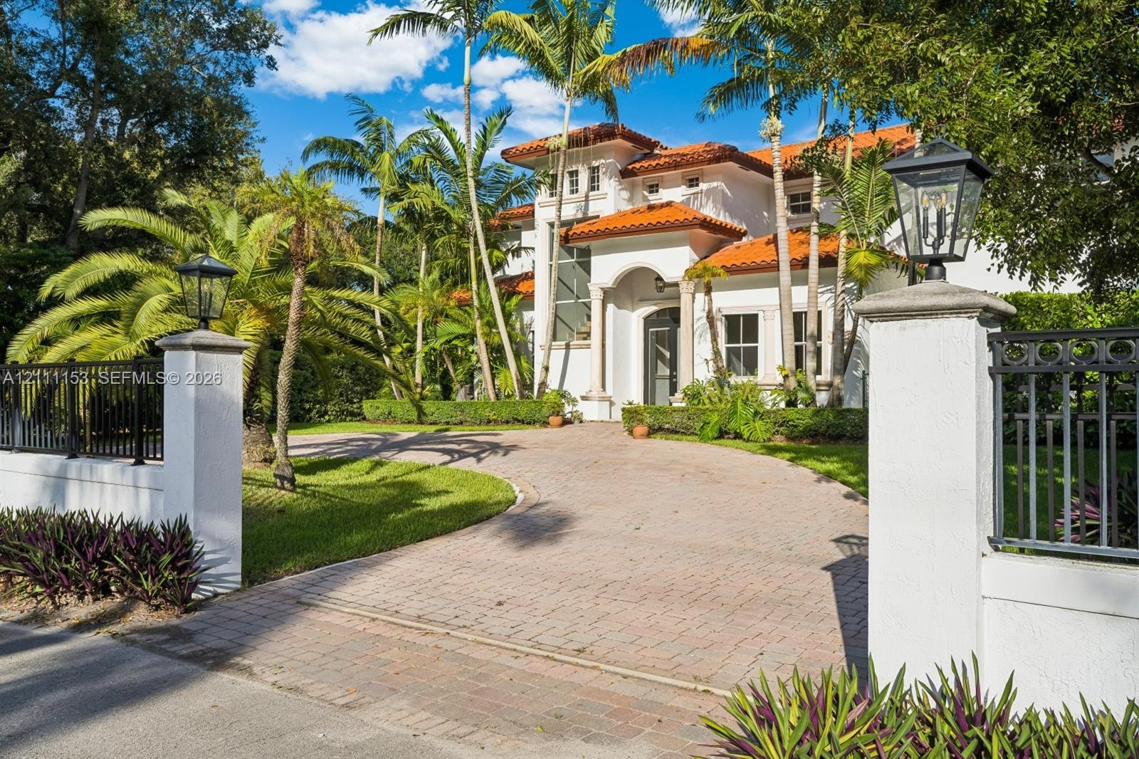 Mediterranean-style residence featuring a terra cotta tile roof, arched entryway with decorative columns, paved driveway, stucco exterior, and gated p