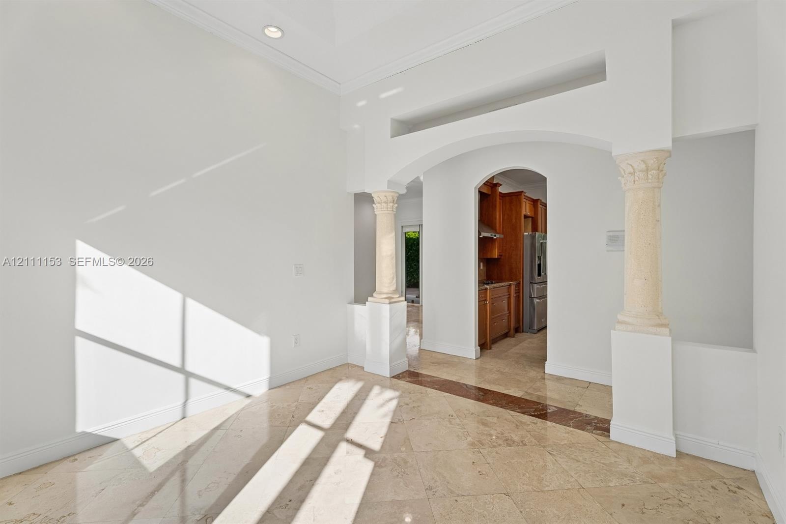 Tray ceiling, stone tile flooring with decorative inlay, arched entryway with dual stone-finish pillars, and recessed lighting