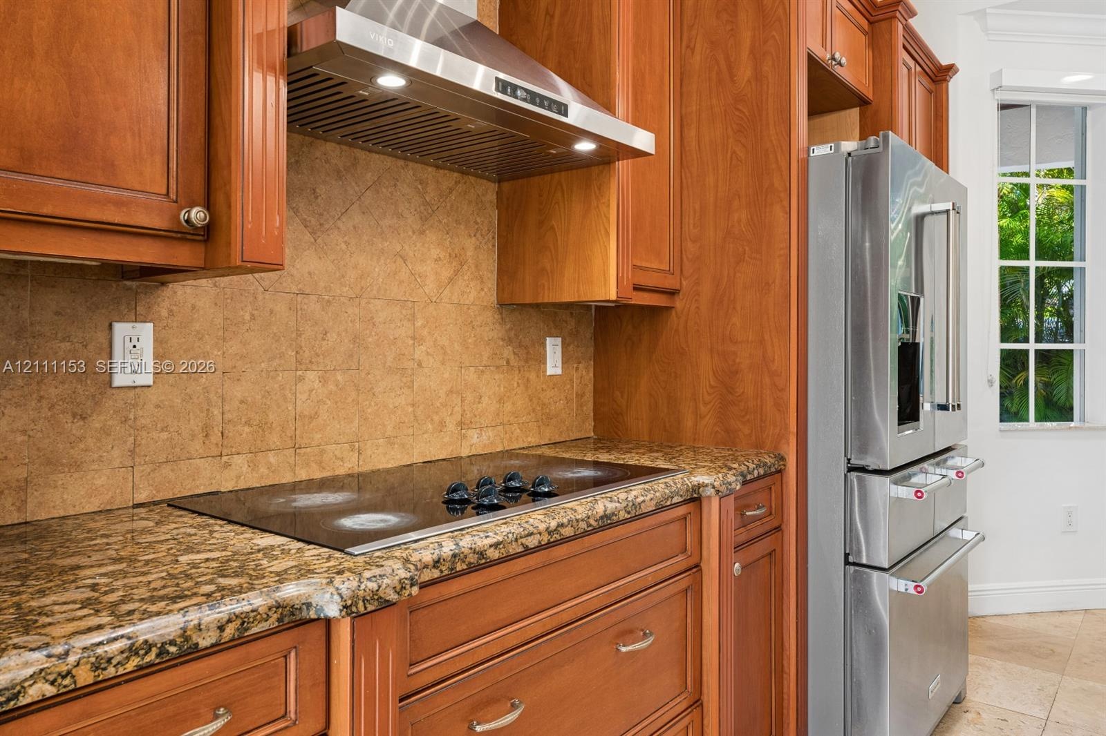 Kitchen featuring wood cabinetry, stone countertops, a glass cooktop, a stainless steel chimney-style range hood, and a stainless steel French door re