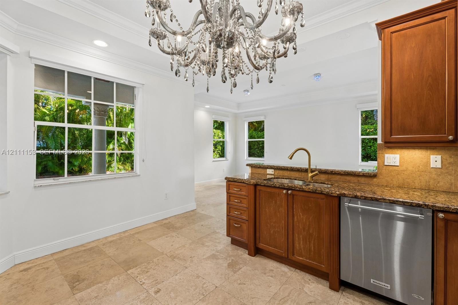 Stone tile flooring, custom wood cabinetry, multi-light crystal chandelier, stainless steel dishwasher, and quartz countertop with an undermount sink