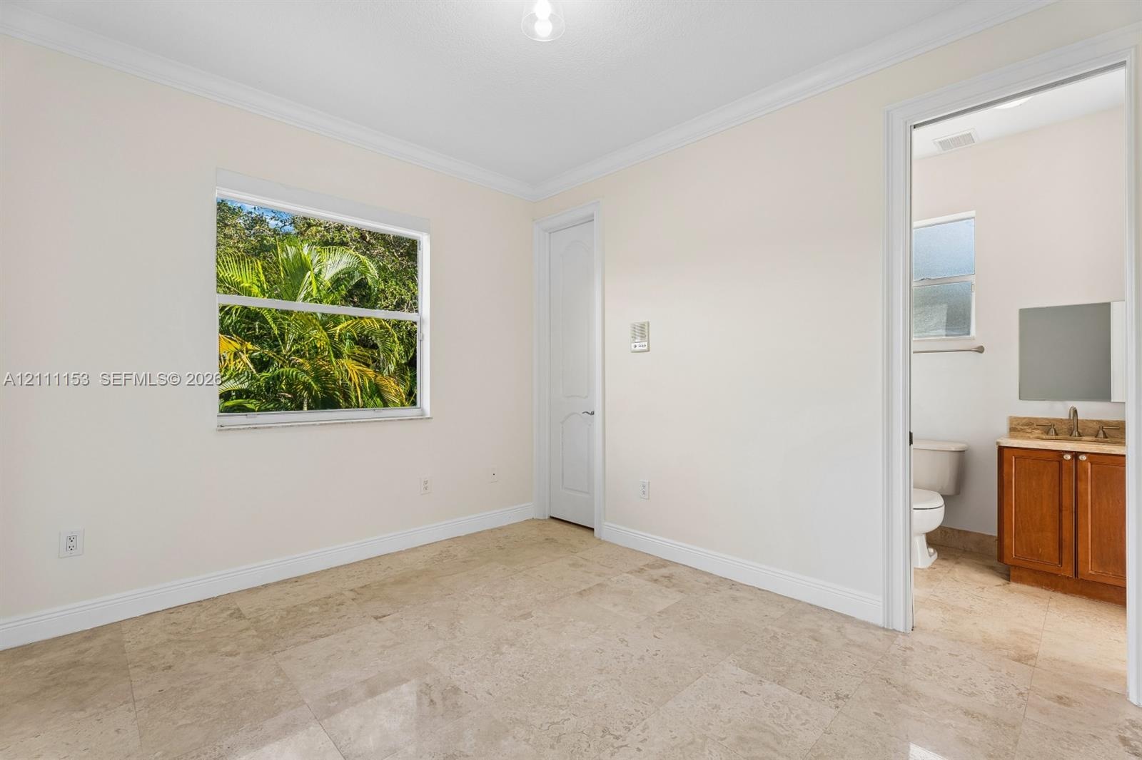 Interior space featuring stone tile flooring, crown molding, a window with exterior greenery, and a doorway revealing a vanity with wood-finish cabine