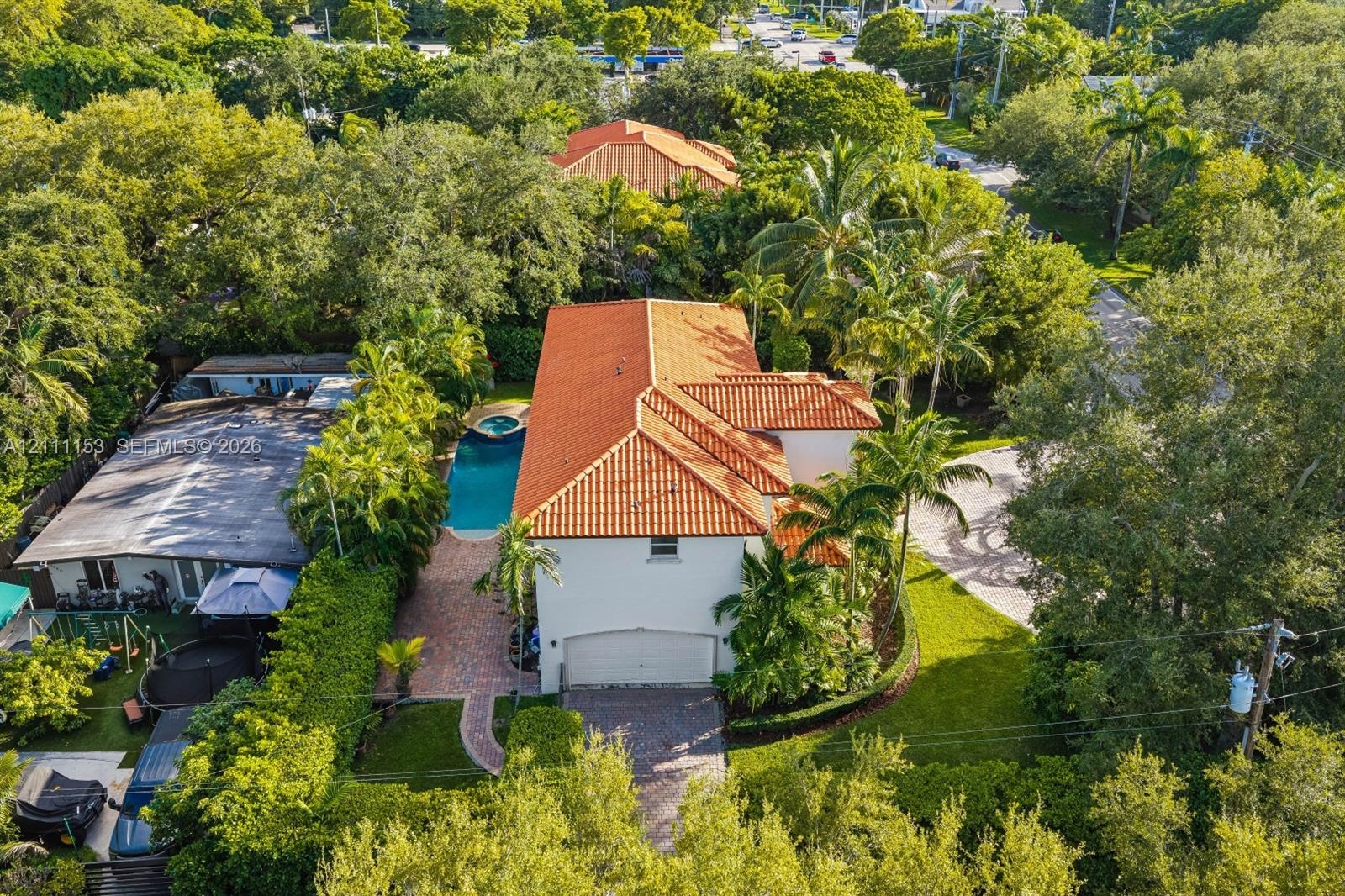 Two-story residence featuring a tile roof, paved driveway, attached garage, in-ground pool with integrated spa, and mature landscaping