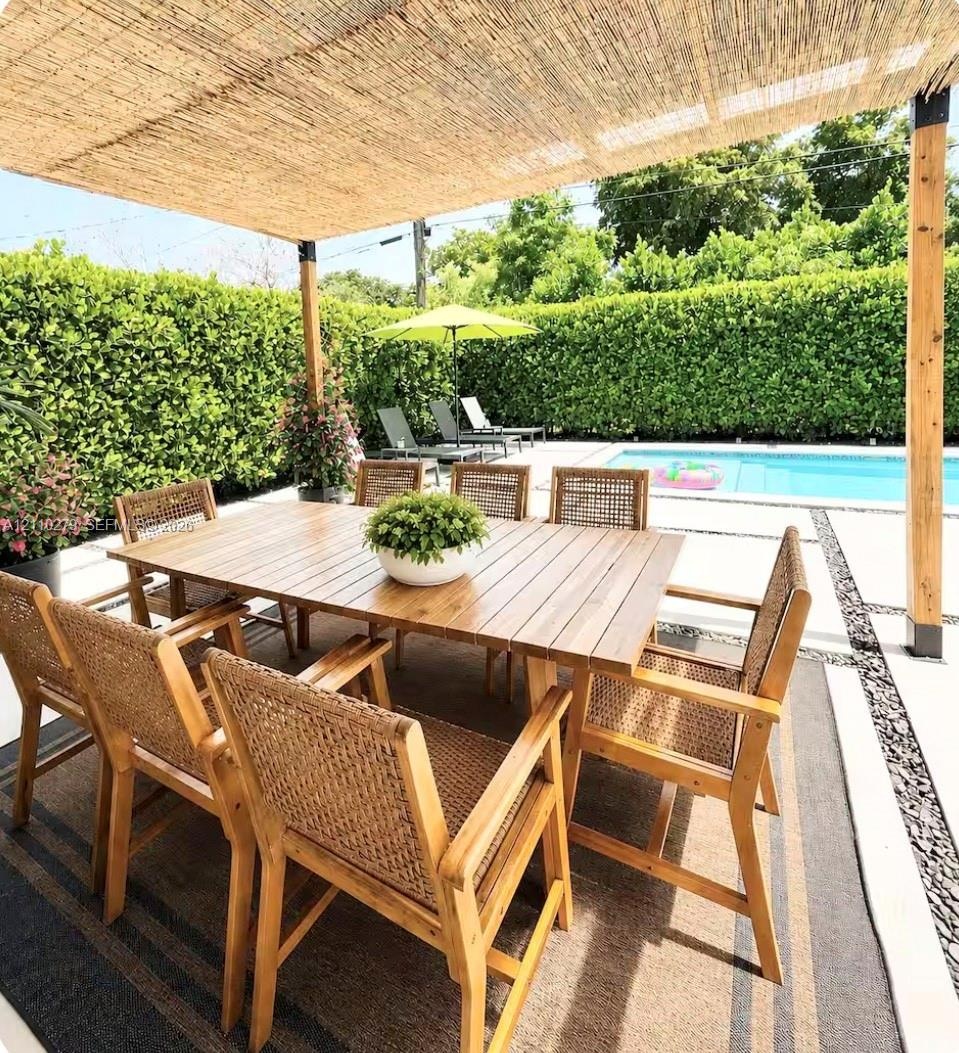 Covered patio featuring a woven reed pergola, concrete paver decking, stone aggregate inlay, and a rectangular swimming pool surrounded by a manicured