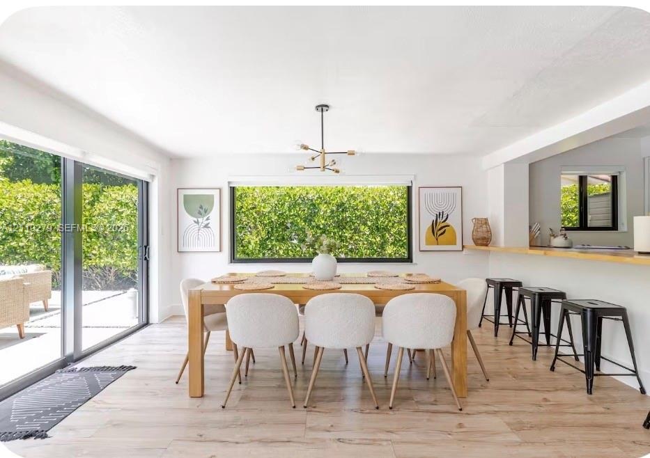 Dining area featuring wood-finish flooring, a contemporary multi-arm chandelier, large sliding glass doors, and a built-in breakfast bar