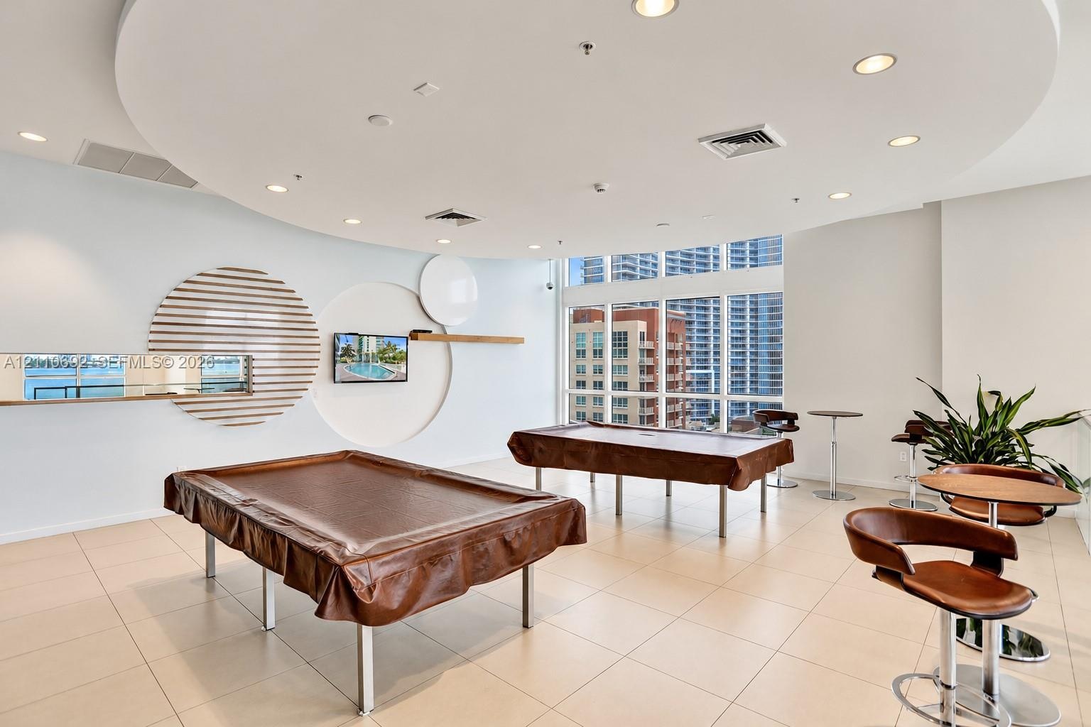 Recreation space featuring large-format tile flooring, a circular dropped ceiling with recessed lighting, floor-to-ceiling windows, and decorative wal