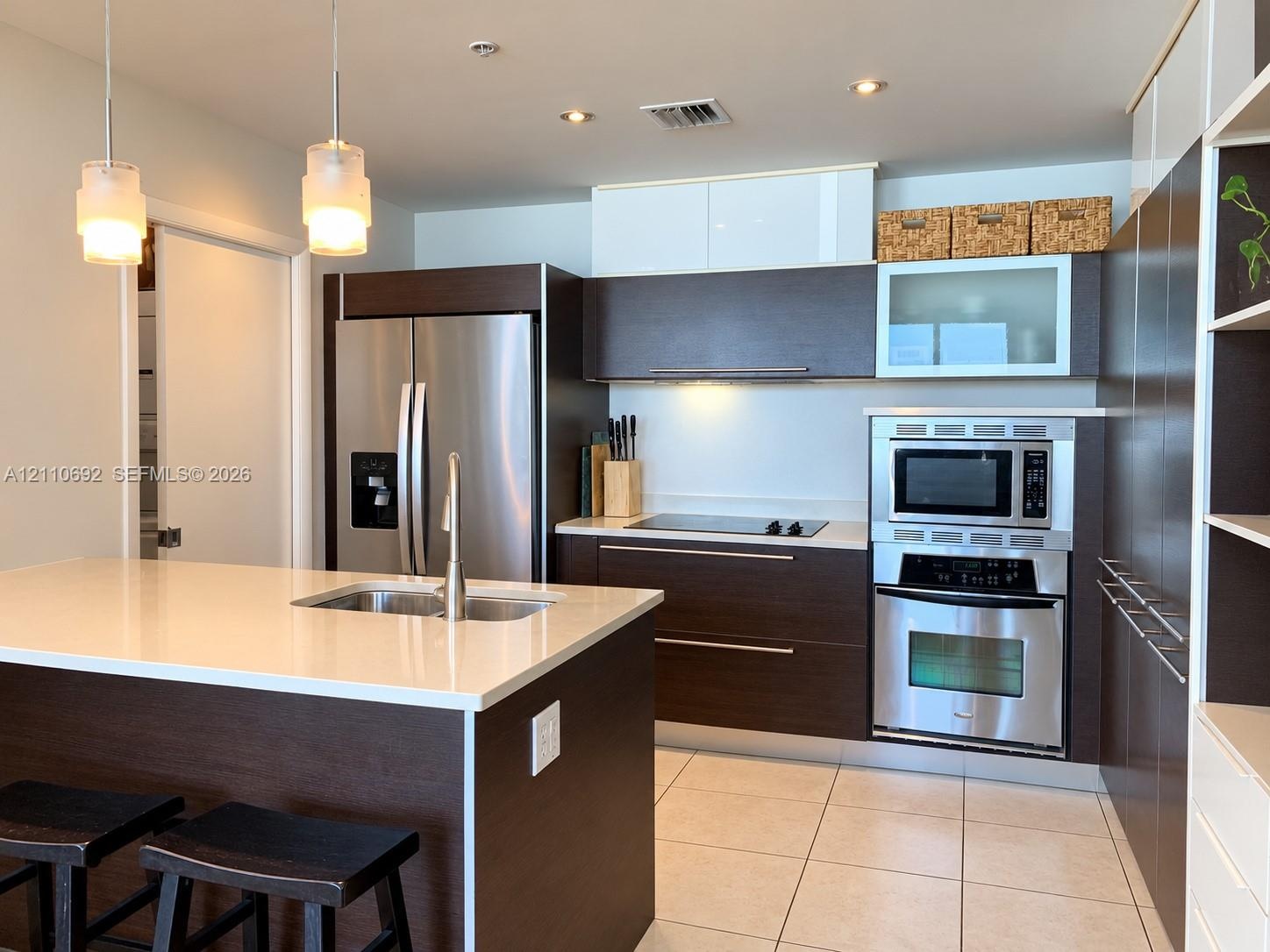 Kitchen featuring dark-finish cabinetry, stone-surface countertops, stainless steel appliances, a central island with a double-basin sink, and recesse