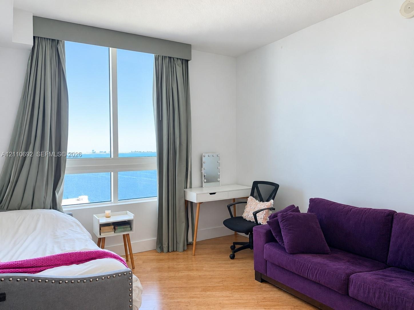 Floor-to-ceiling windows featuring expansive coastal scenery, wood-finish flooring, and a neutral color palette