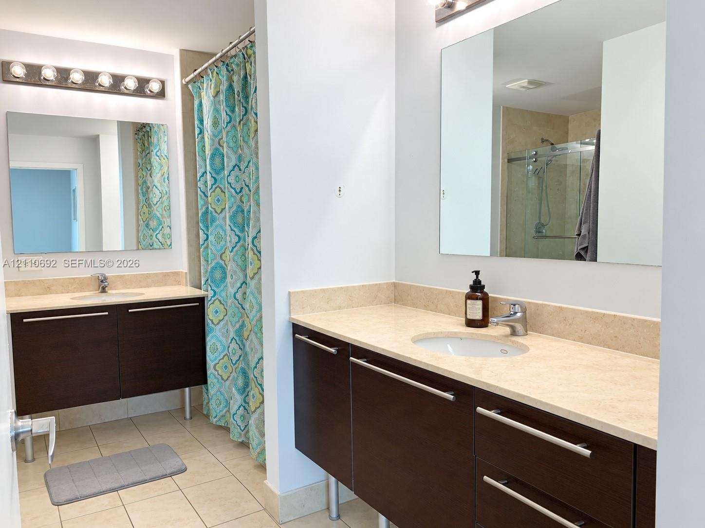 Dual floating vanities featuring dark wood-finish cabinetry, light-toned stone countertops, undermount sinks, and polished hardware, complemented by f