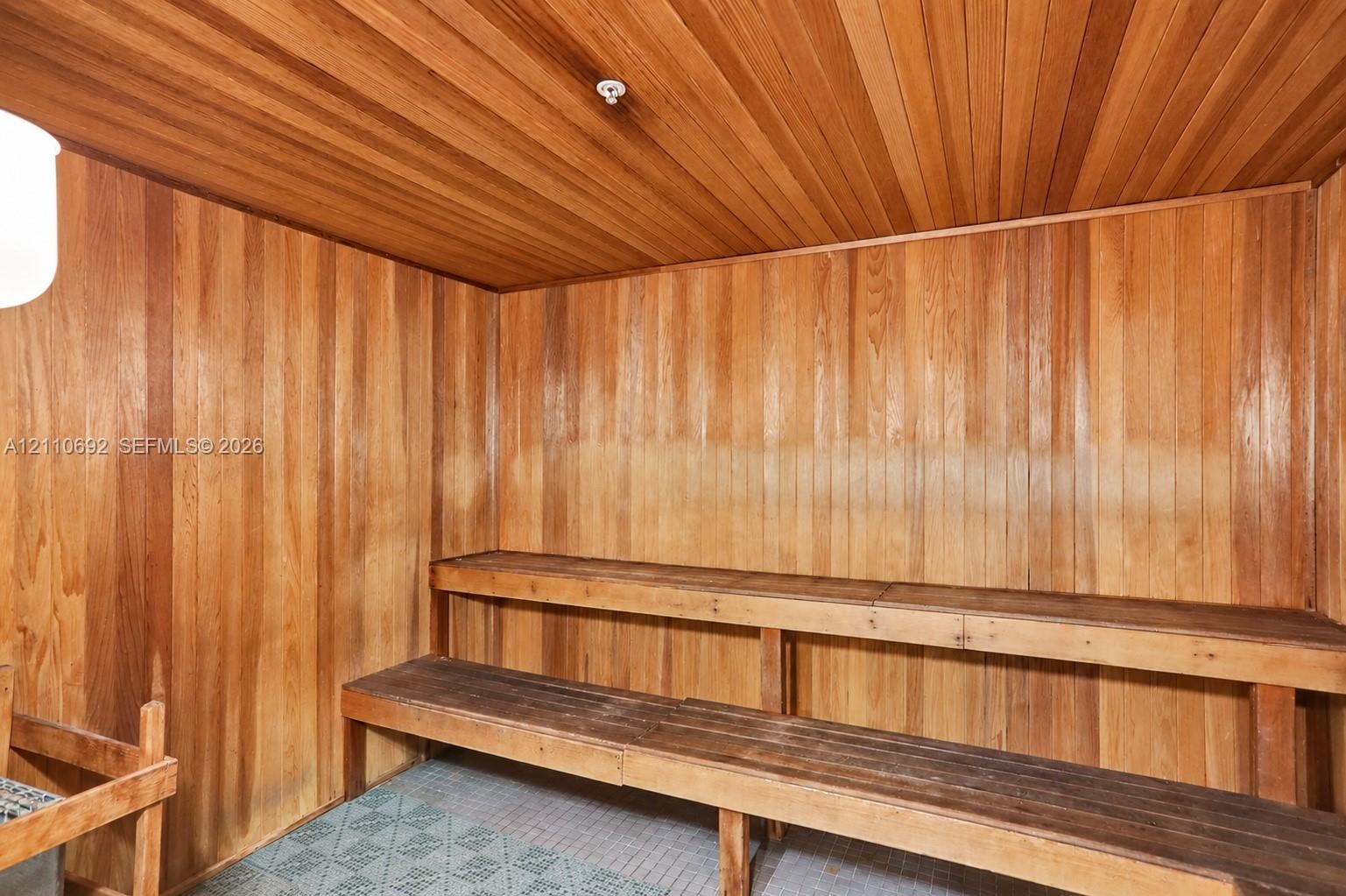 Sauna featuring vertical wood wall paneling, horizontal wood ceiling slats, dual-level wood bench seating, and tile flooring
