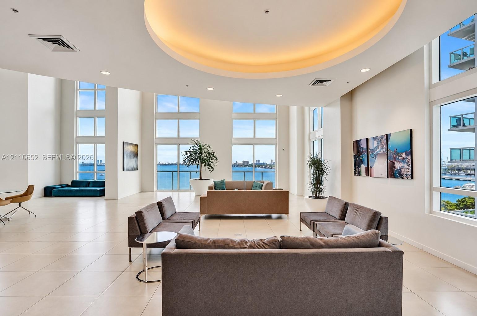 Expansive open-concept room featuring floor-to-ceiling windows, polished tile flooring, a recessed circular tray ceiling with integrated lighting, and