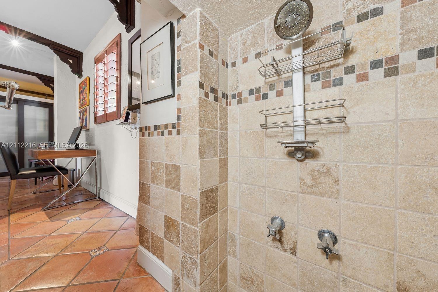 Shower stall featuring square-cut natural stone wall tile, decorative mosaic accent banding, a chrome-finish shower head, and dual-handle wall-mounted