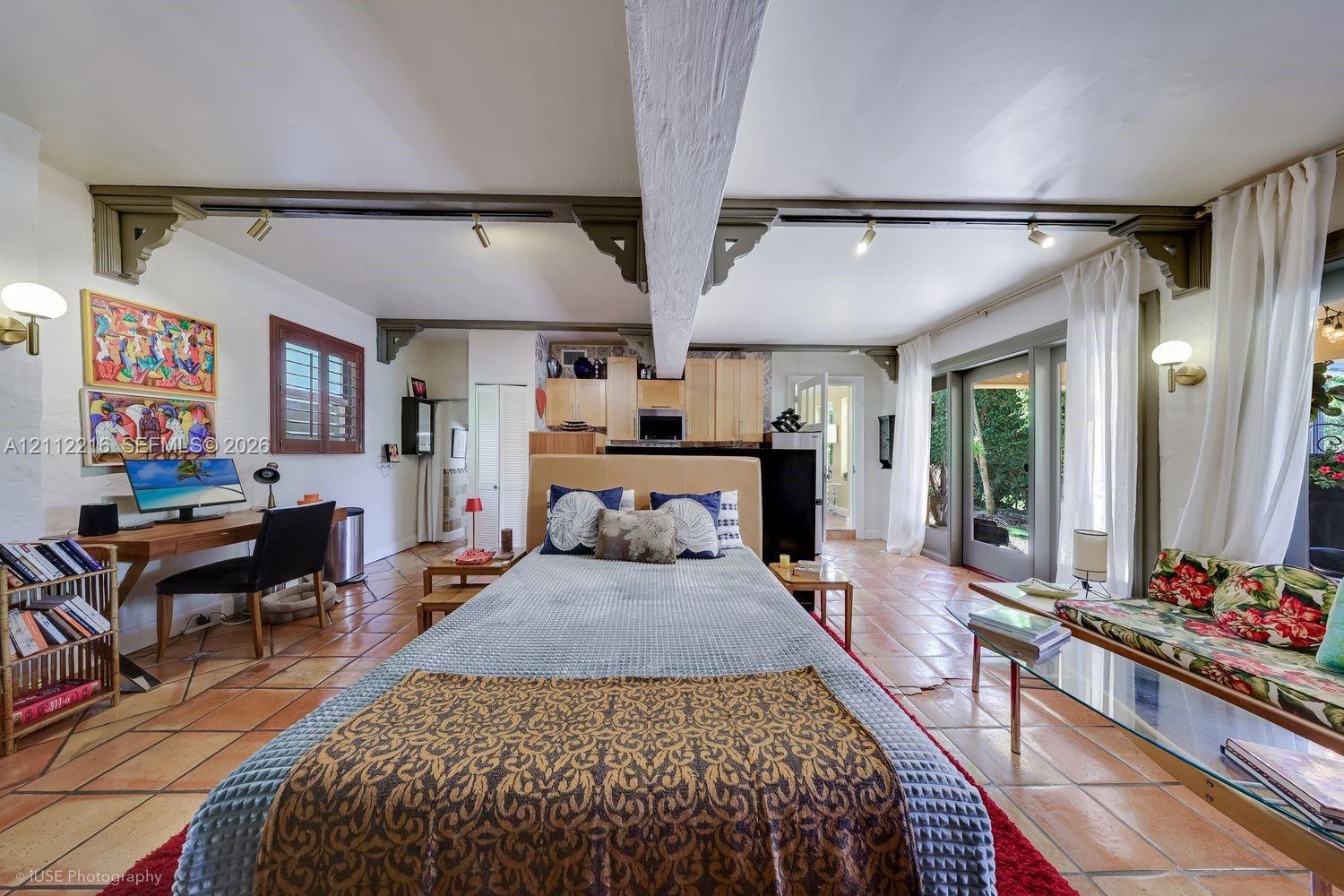 Spacious interior featuring terra cotta tile flooring, exposed structural beams with decorative corbel accents, track lighting, and sliding glass door