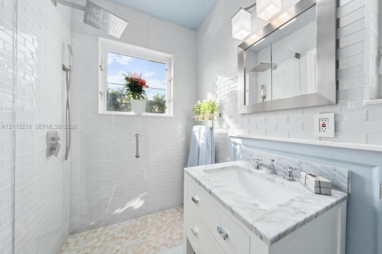 Bathroom featuring a white vanity with a stone countertop, a glass-enclosed shower with pebble-stone flooring, subway tile wall cladding, and a framed