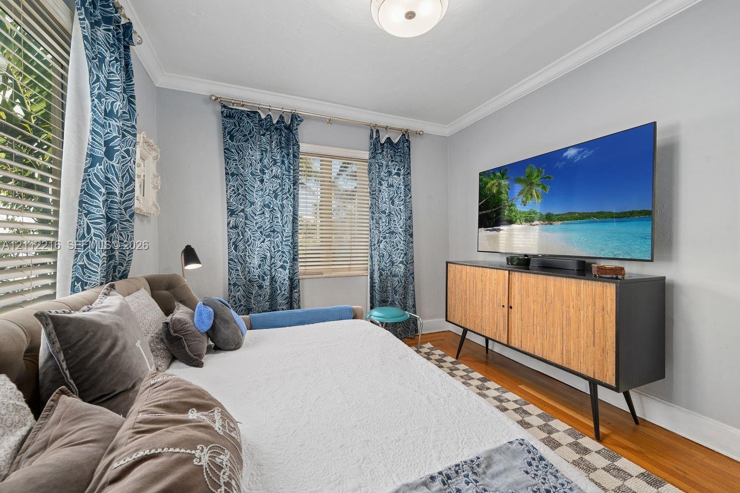 Room featuring wood-finish flooring, crown molding, and two windows with horizontal blinds and metal curtain rods