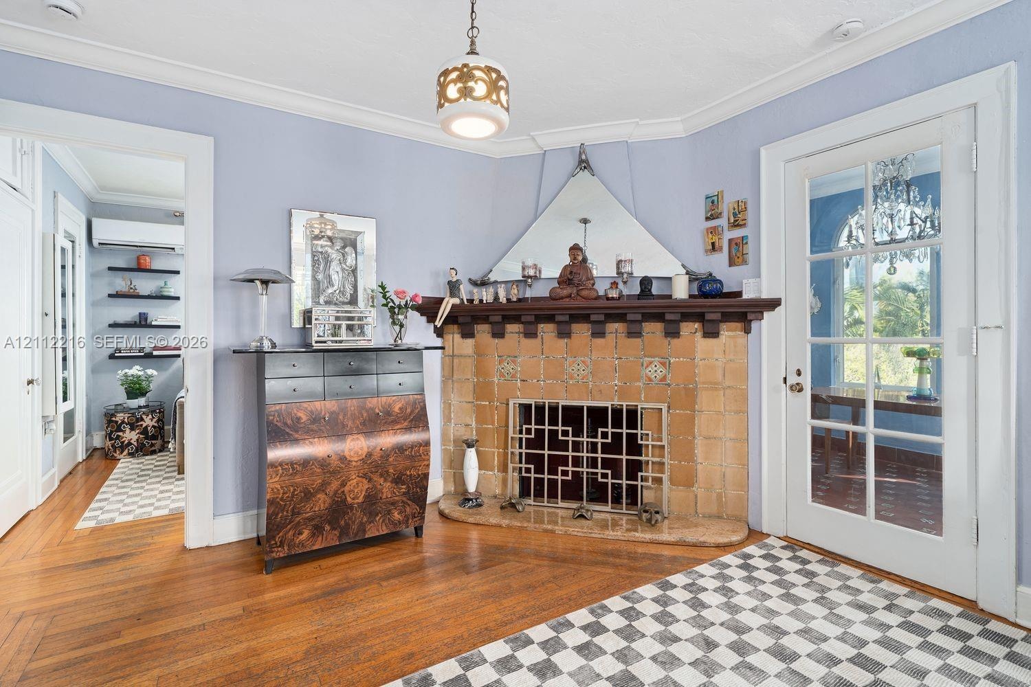 Corner fireplace featuring a detailed tile surround, dark wood mantel, and metal hearth screen, complemented by polished wood-finish flooring and a gl