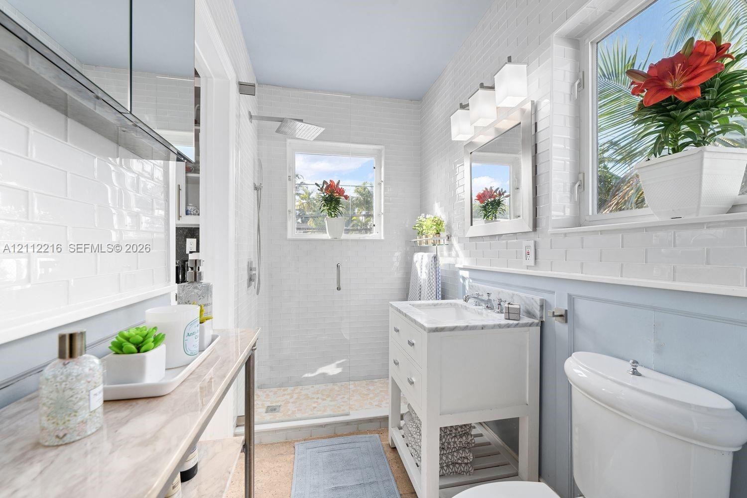 Bathroom featuring white subway tile wall cladding, a walk-in shower with a rainfall showerhead, a freestanding vanity with a stone countertop, and po