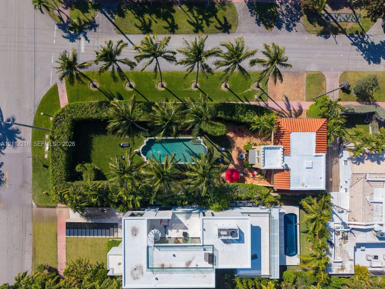 Aerial perspective of a multi-structure property featuring a swimming pool, a second elongated swimming pool, expansive manicured lawn, and mature per