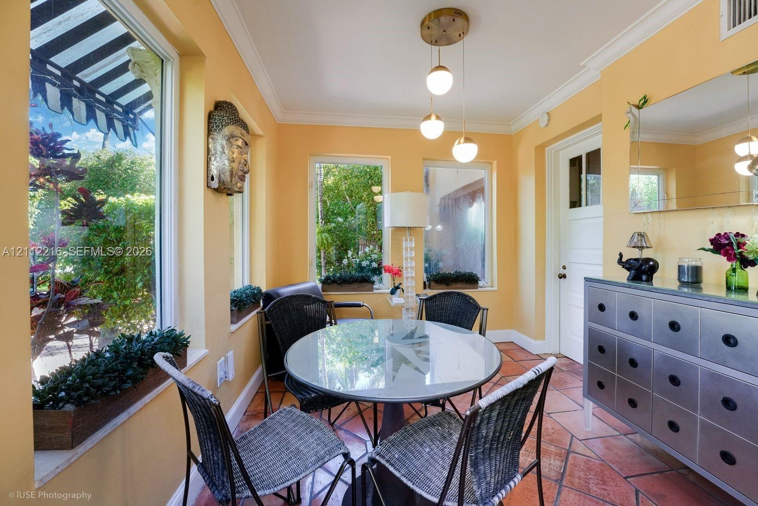 Sunroom featuring terracotta tile flooring, crown molding, multi-pane windows, and a three-light modern pendant fixture