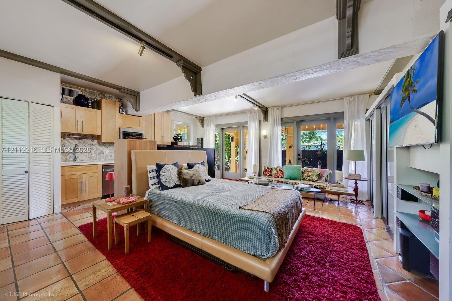 Open-concept living space featuring terracotta tile flooring, exposed structural beams with decorative corbels, natural wood cabinetry, patterned tile