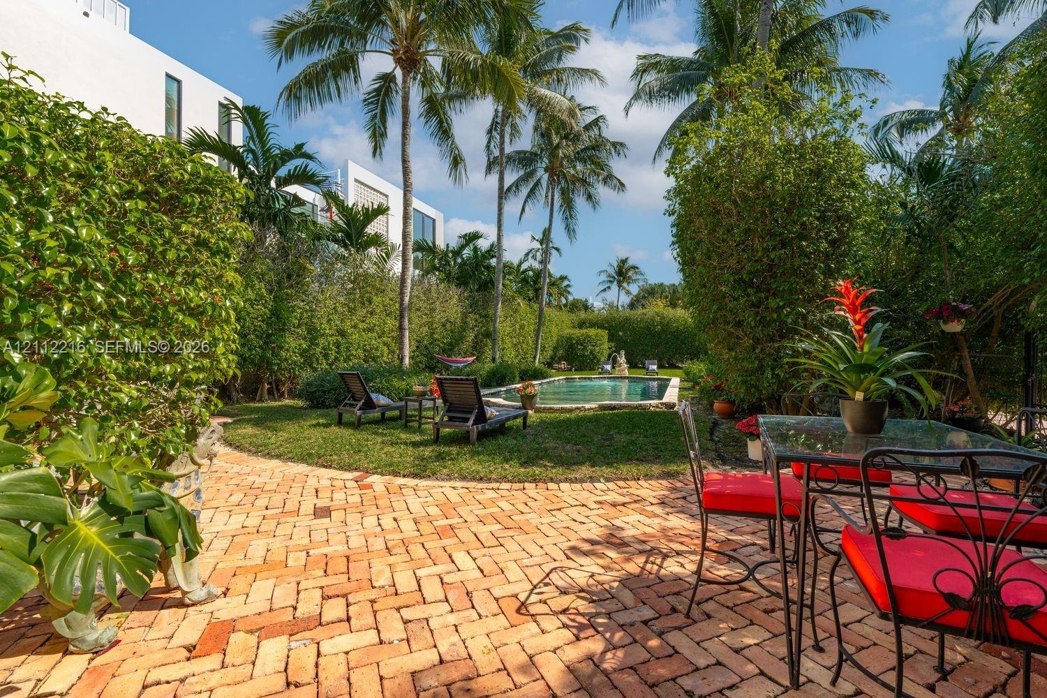Private backyard featuring a brick patio, in-ground swimming pool, manicured lawn, and mature palm trees enclosed by tall hedging