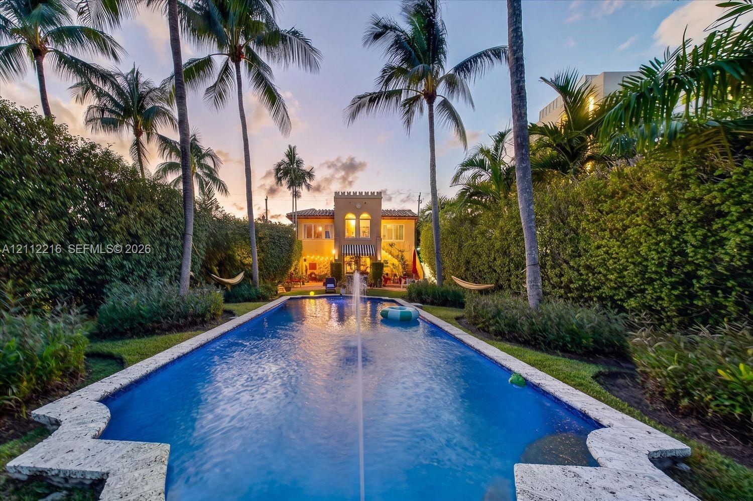 Rectangular swimming pool with a central fountain feature, stone-finished coping, and palm tree landscaping