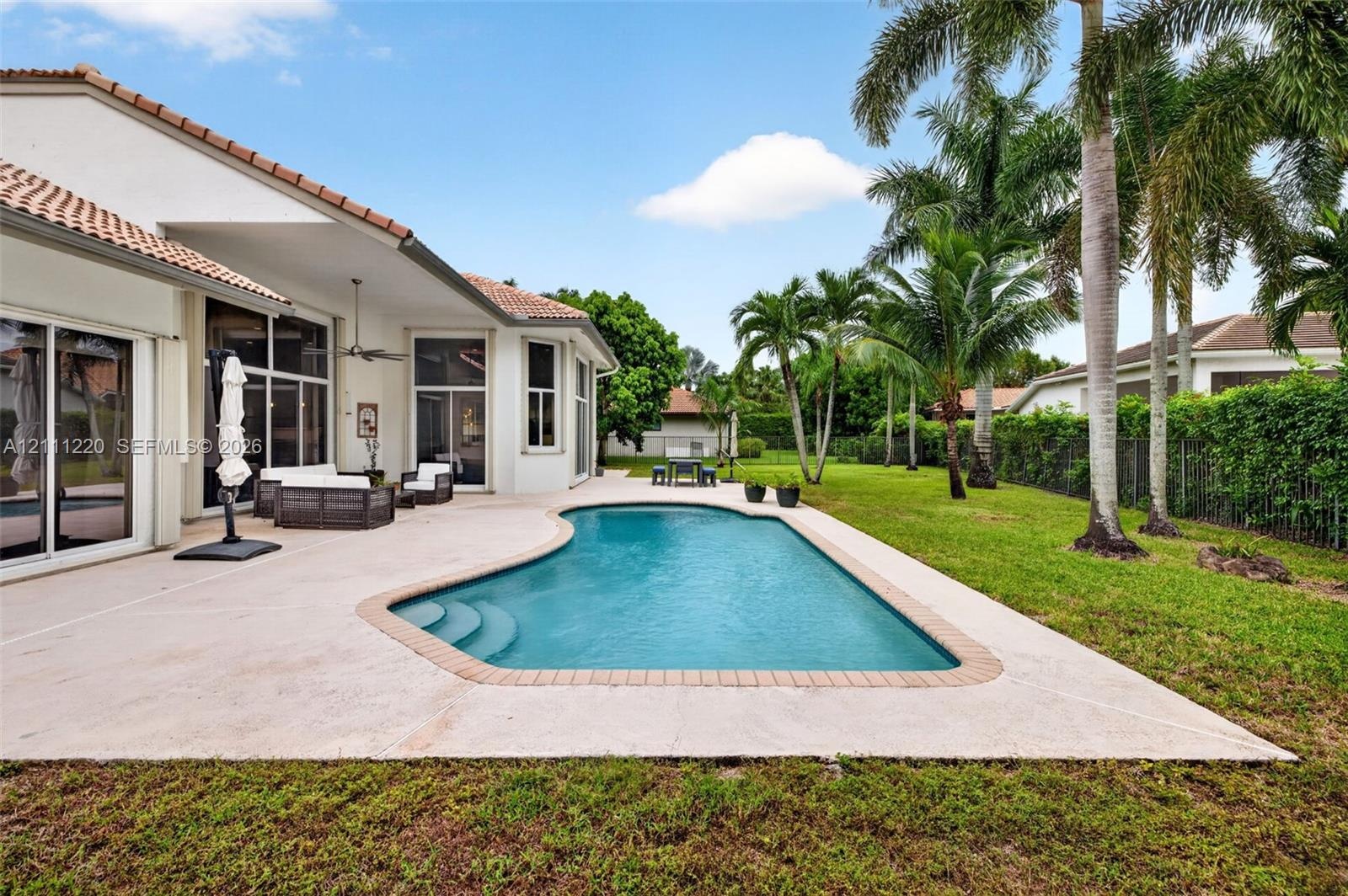 Expansive concrete patio featuring a built-in pool with masonry coping, mature palms, and manicured lawn