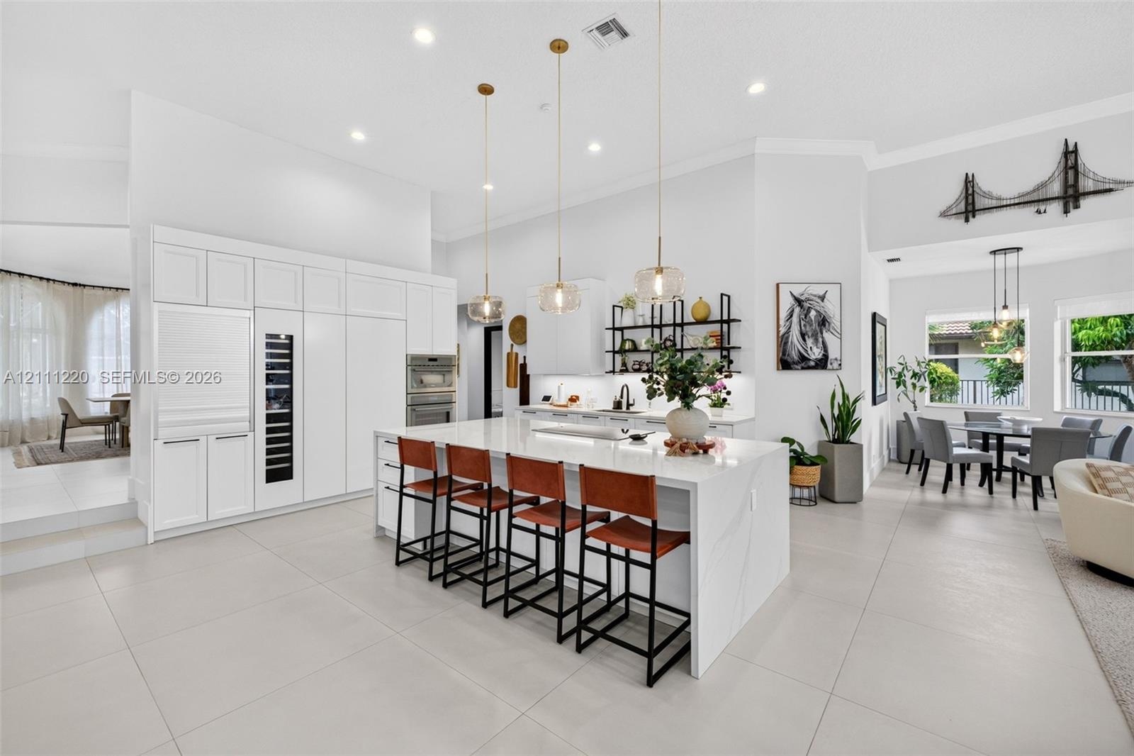 Gourmet kitchen featuring a large central island with stone-finish countertops, custom floor-to-ceiling white cabinetry, integrated stainless steel ap