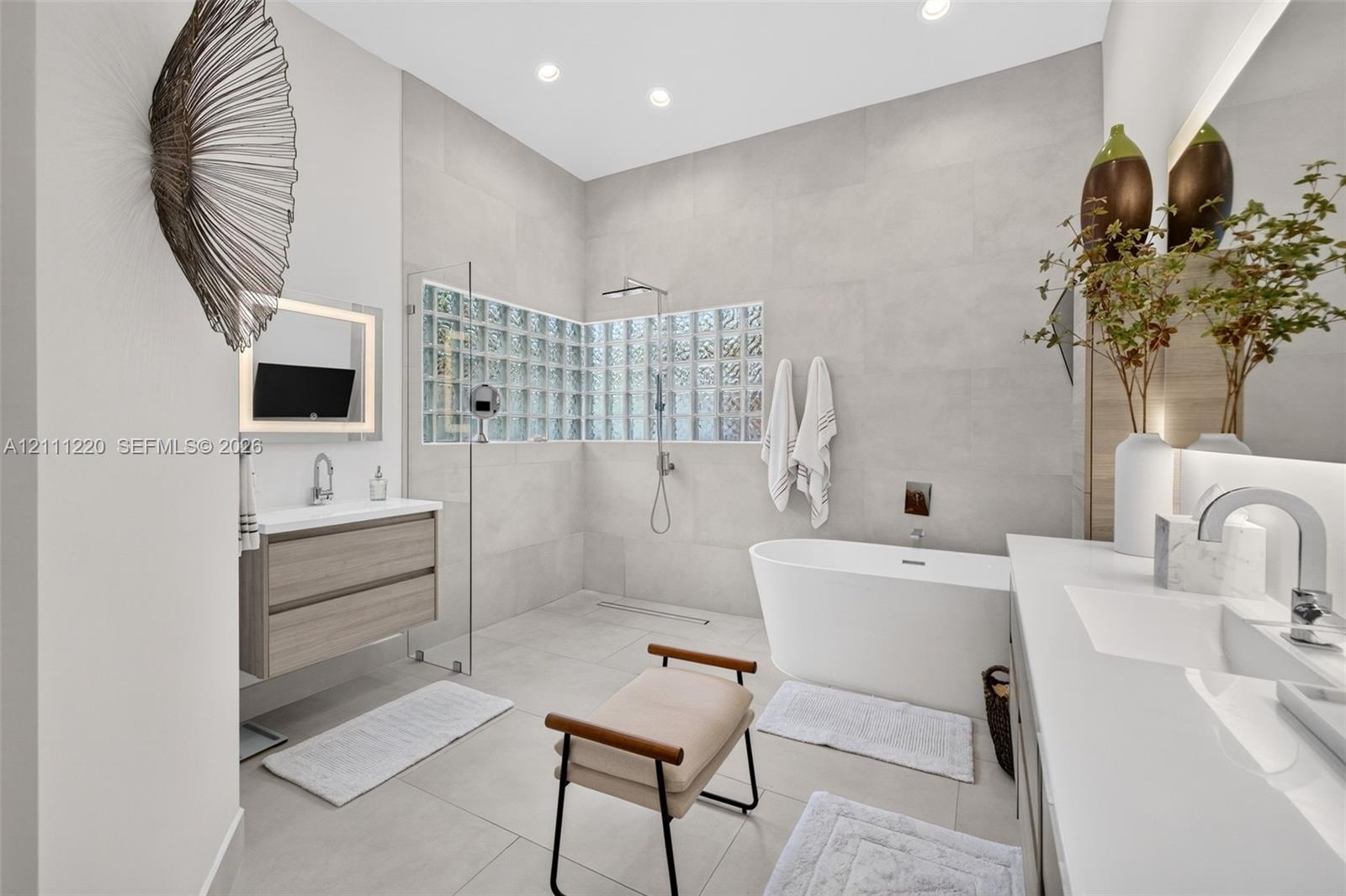 Bathroom featuring a freestanding soaking tub, glass-enclosed shower with glass block accent wall, wall-mounted wood-finish vanity, and integrated LED