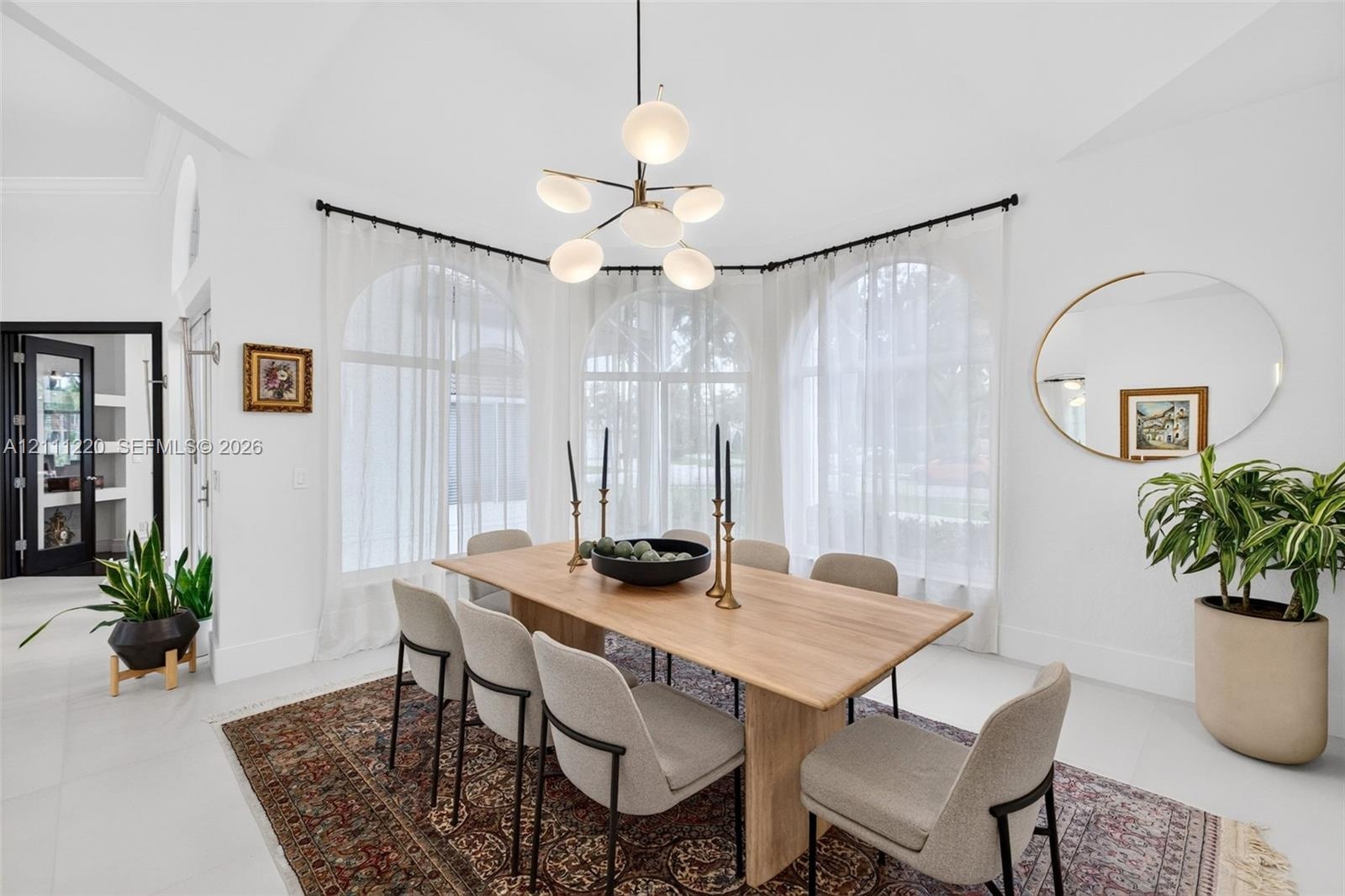 Dining area featuring three large arched windows, vaulted ceiling, and a modern multi-globe chandelier with a metal finish