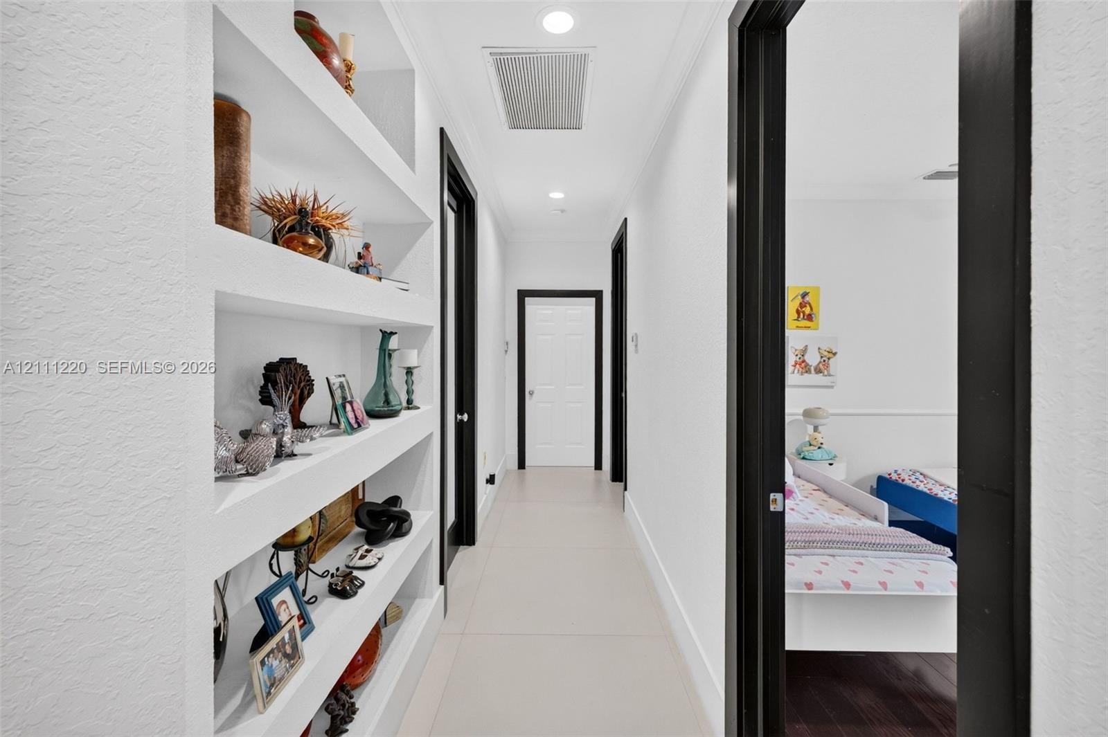 Hallway featuring built-in recessed wall shelving, high-contrast dark door casings, smooth wall finish, and neutral tile flooring