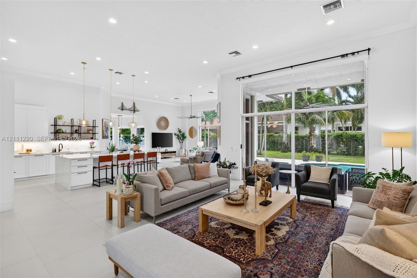 Open-concept living area featuring large-format tile flooring, high ceilings with recessed lighting, kitchen with white cabinetry and a center island,