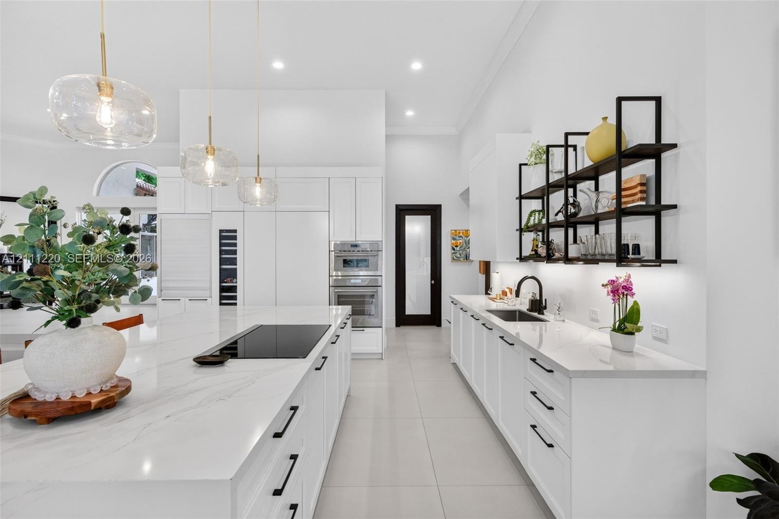 Modern kitchen featuring a stone-surface island with an integrated induction cooktop, white cabinetry with matte black hardware, stainless steel doubl