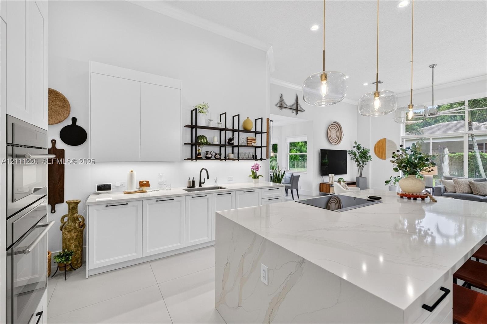 Kitchen featuring a large central island with a stone-surface countertop, high-gloss white cabinetry, built-in stainless steel double wall ovens, matt
