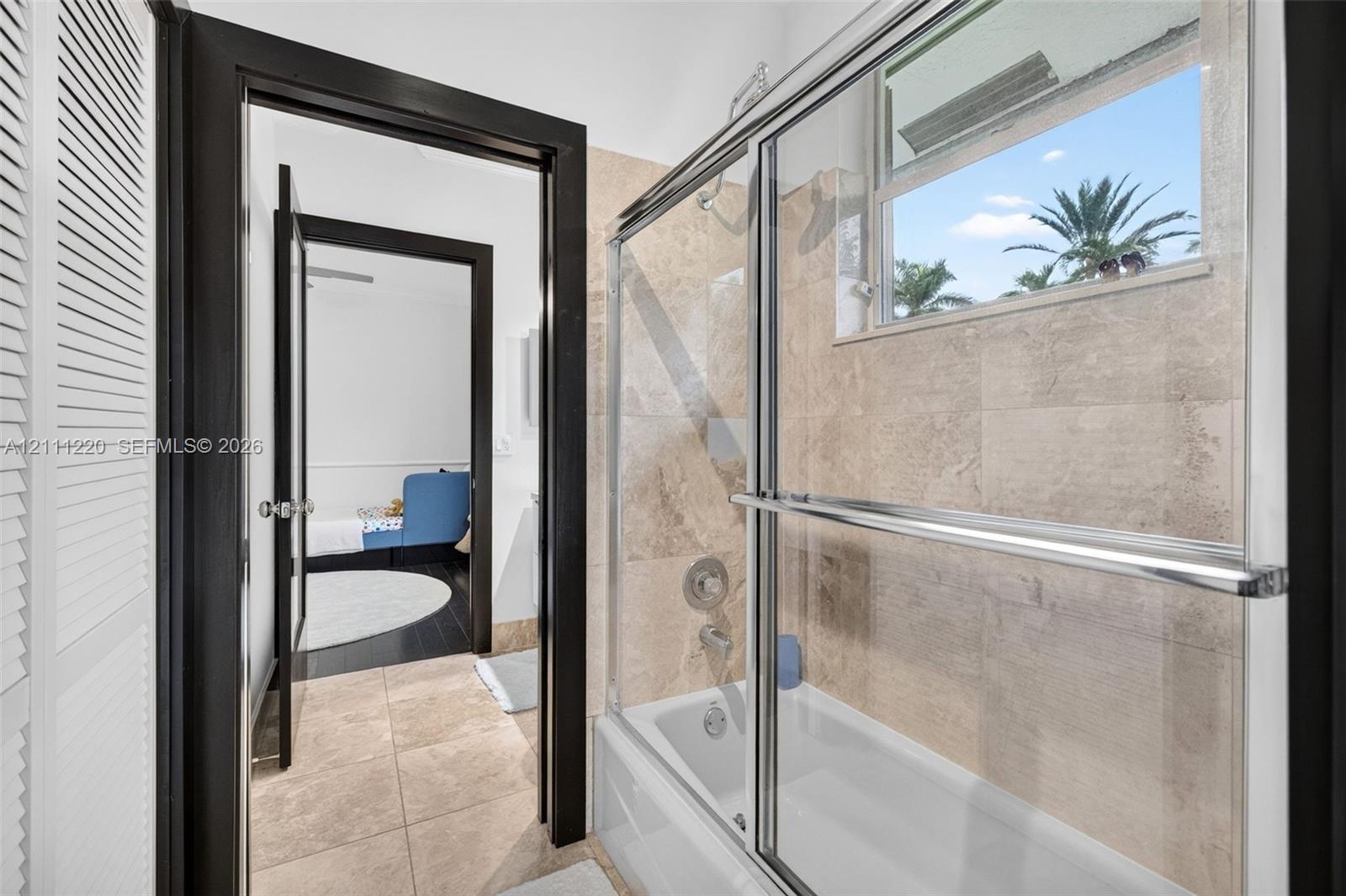 Full bathroom featuring a tub-shower combination with a sliding glass enclosure, large-format stone-finish wall and floor tiling, and dark-finished do