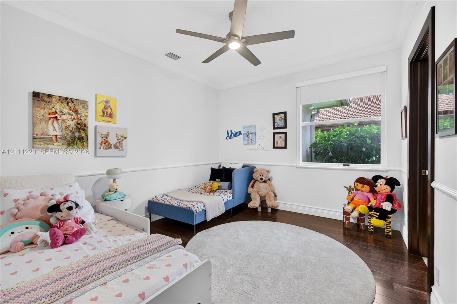 Bedroom interior featuring dark wood-finish flooring, crown molding, chair rail trim, a multi-blade ceiling fan with integrated lighting, and a single