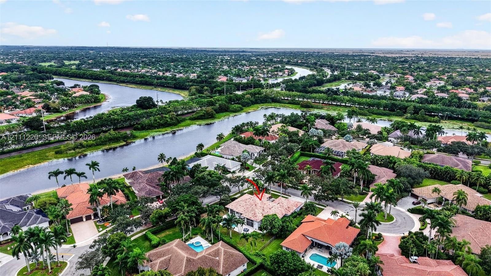 Aerial perspective of a property featuring a multi-pitched tile roof, mature perimeter landscaping, and a waterfront location