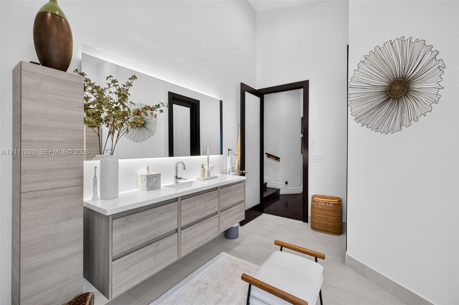 Floating vanity with wood-finish cabinetry, solid-surface countertop, integrated rectangular sink, wall-to-wall mirror with integrated LED backlightin