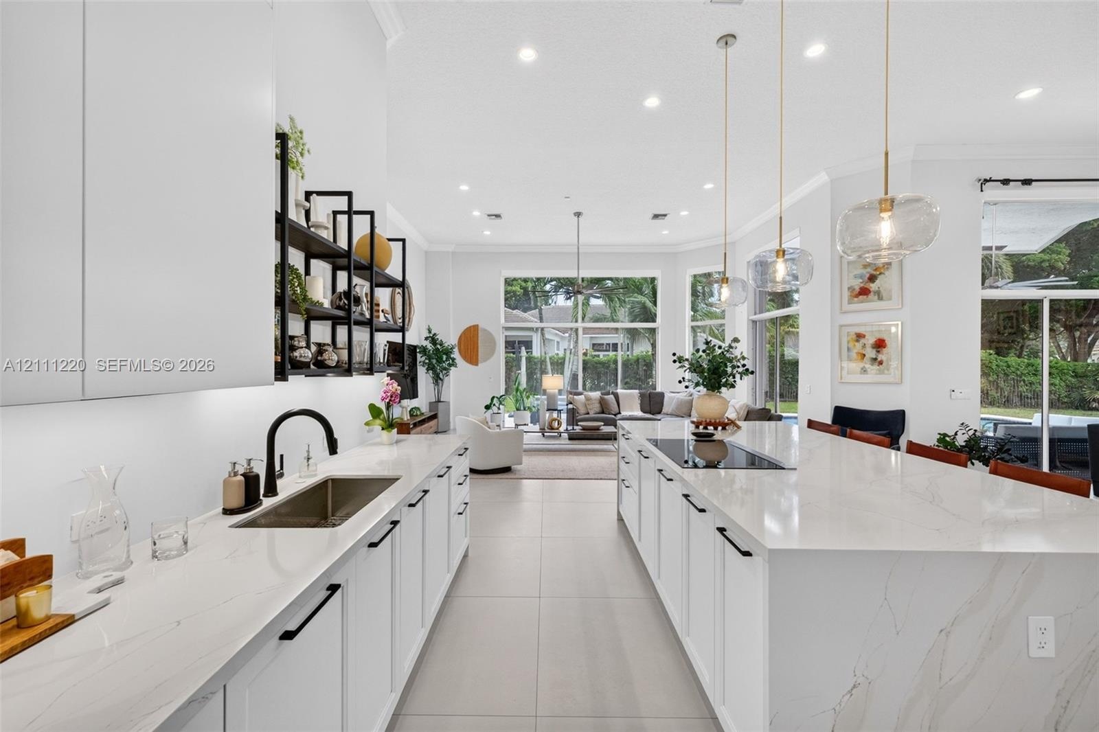 Kitchen featuring expansive central island with quartz surfacing, integrated cooktop, recessed lighting, matte black hardware, and open shelving