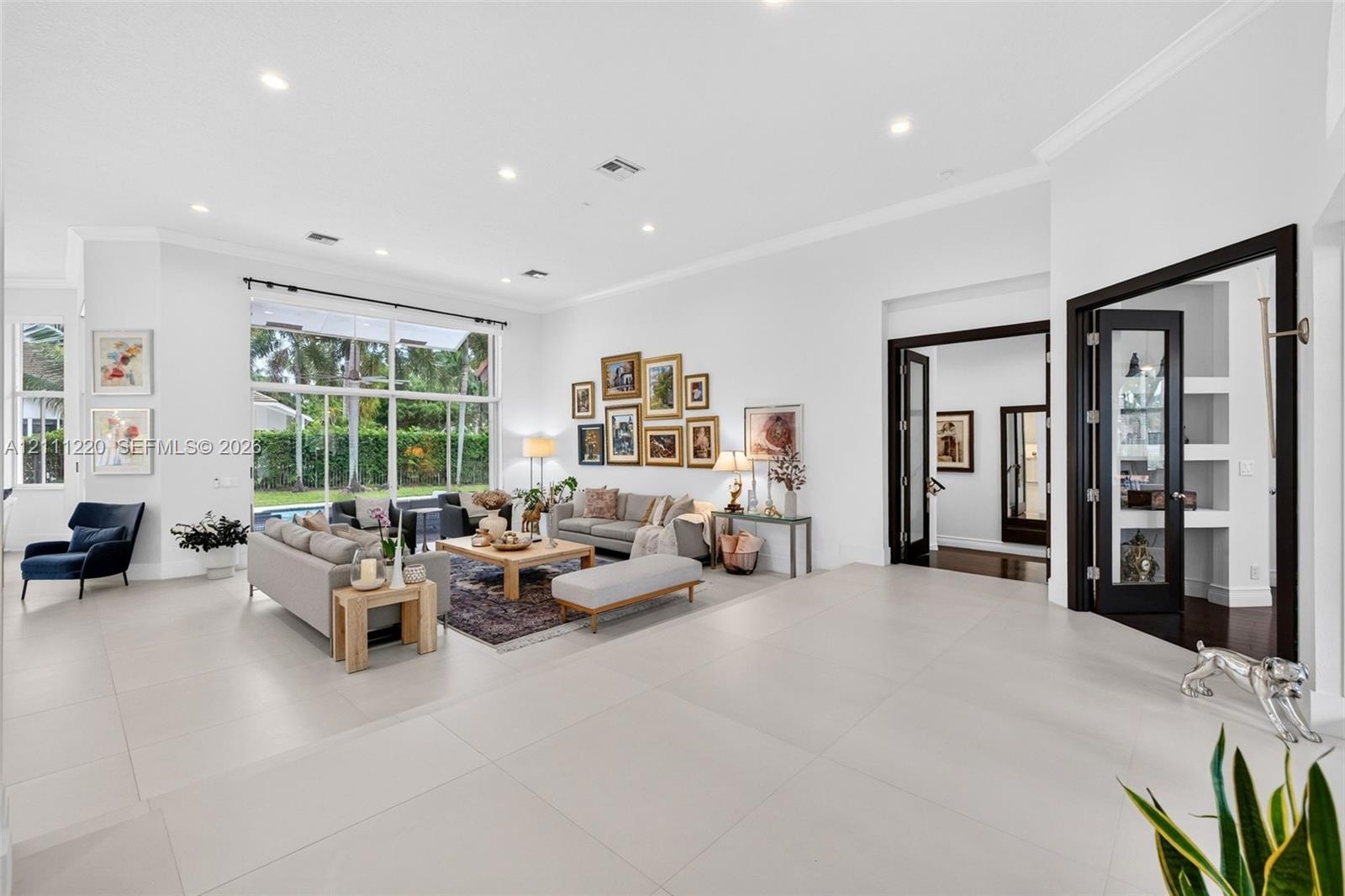 Spacious interior featuring large-format tile flooring, recessed lighting, expansive floor-to-ceiling windows, and French doors with dark-finished tri