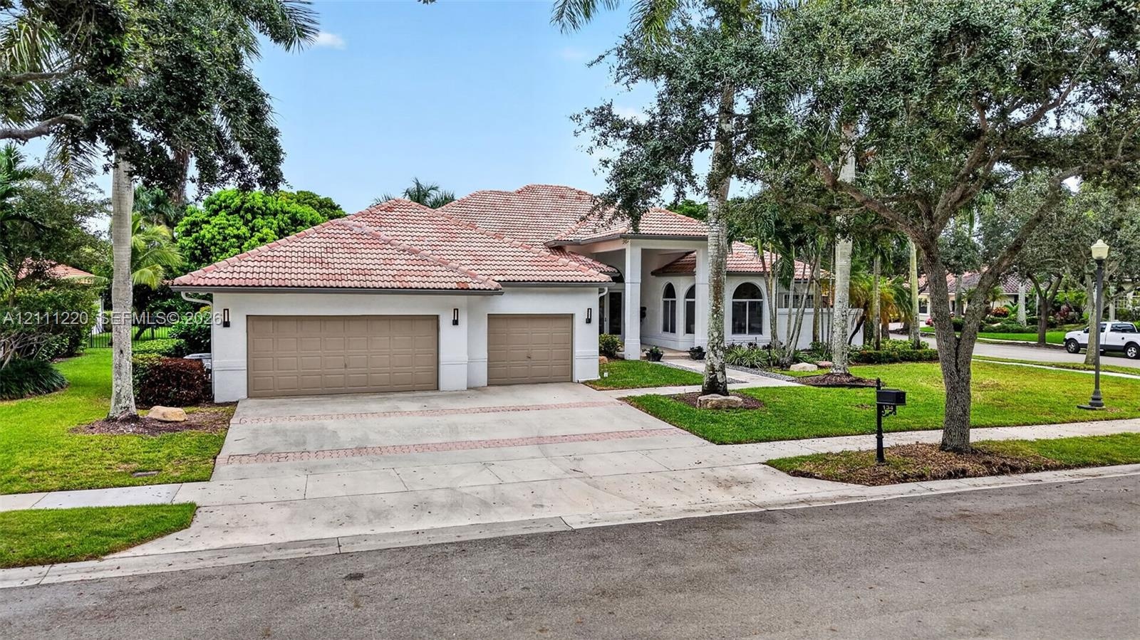 Exterior featuring a multi-gabled tile roof, stucco facade, arched windows, and a three-car garage with a paved driveway